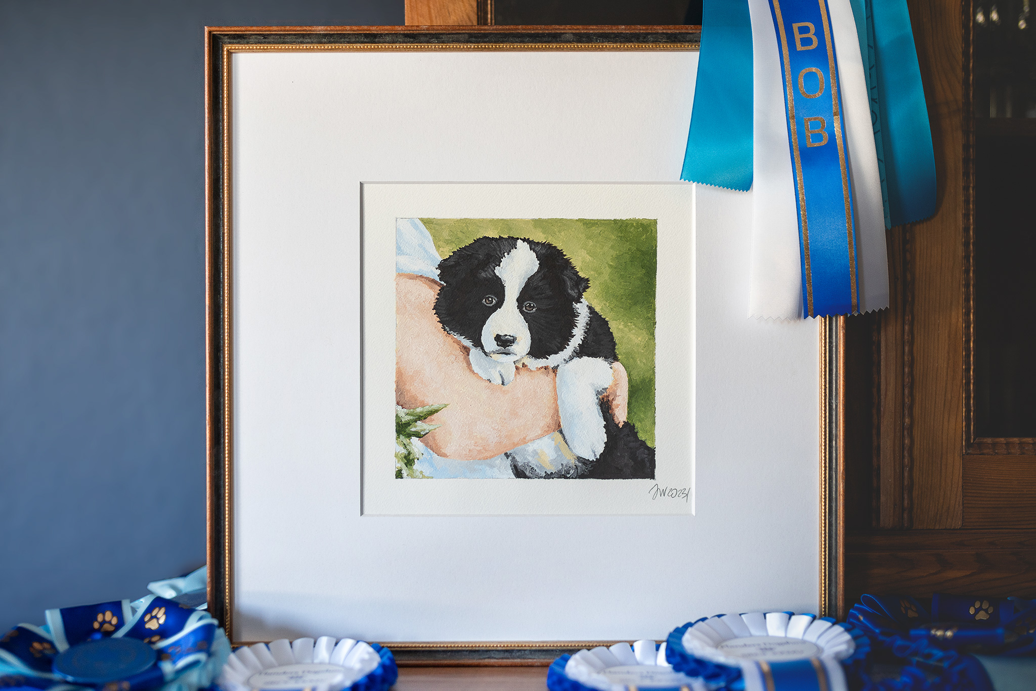 Gemalter Border Collie Welpe in einem braunen Rahmen mit blauen Siegerschleifen